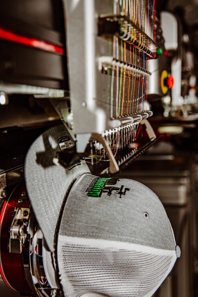 An embroidered cap is positioned under a high-tech embroidery machine